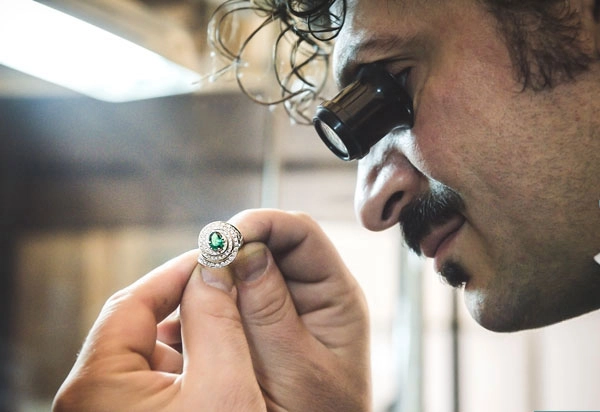 Antonio Colonna looking at a green-stoned ring through a jeweller's loupe
