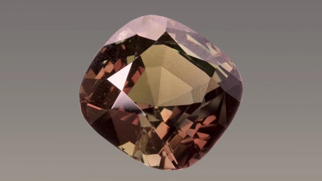 Alessandrite taglio cuscino fotografata in primo piano, con tonalità bruno rosata e riflessi sfaccettati.