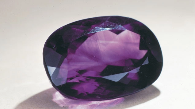 Ametista ovale sfaccettata con colore viola profondo, fotografata in primo piano.