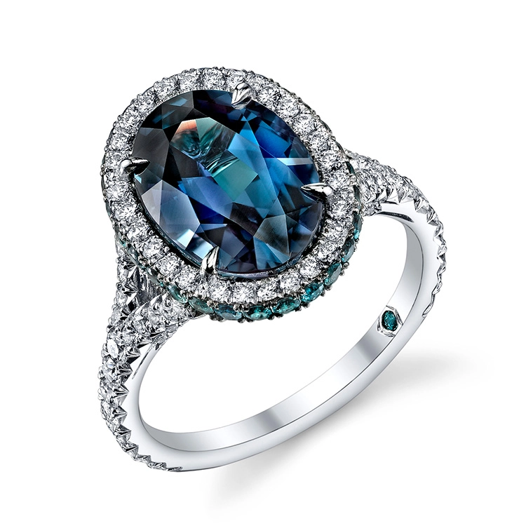 Anello con grande alessandrite ovale blu verde, contorno di diamanti e montatura in metallo bianco.