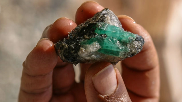Smeraldo grezzo su roccia tenuto in mano